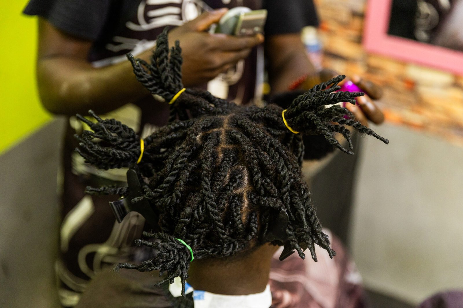 A man with dreadlocks is getting her hair cut by a barber in his barbershop.