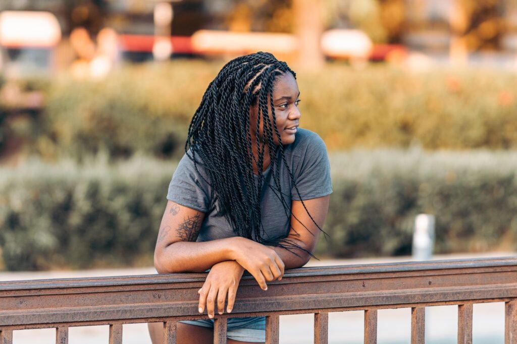Distracted afro woman with braided hair leaning on a rail in the street